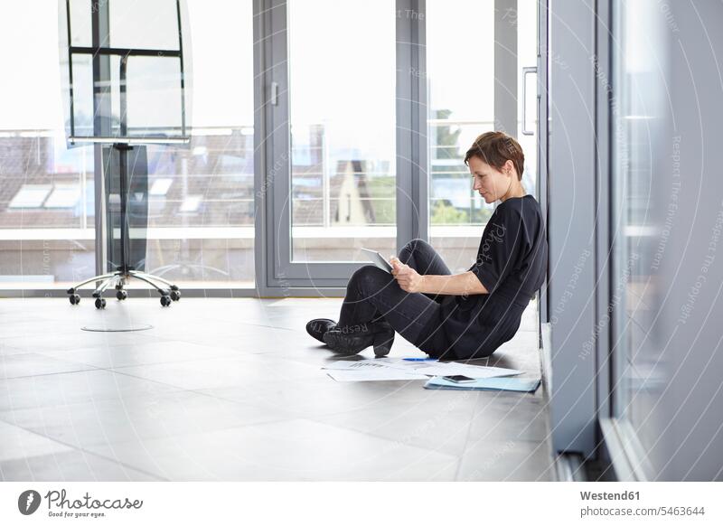 Businesswoman sitting on the floor in office using tablet Seated floors offices office room office rooms businesswoman businesswomen business woman