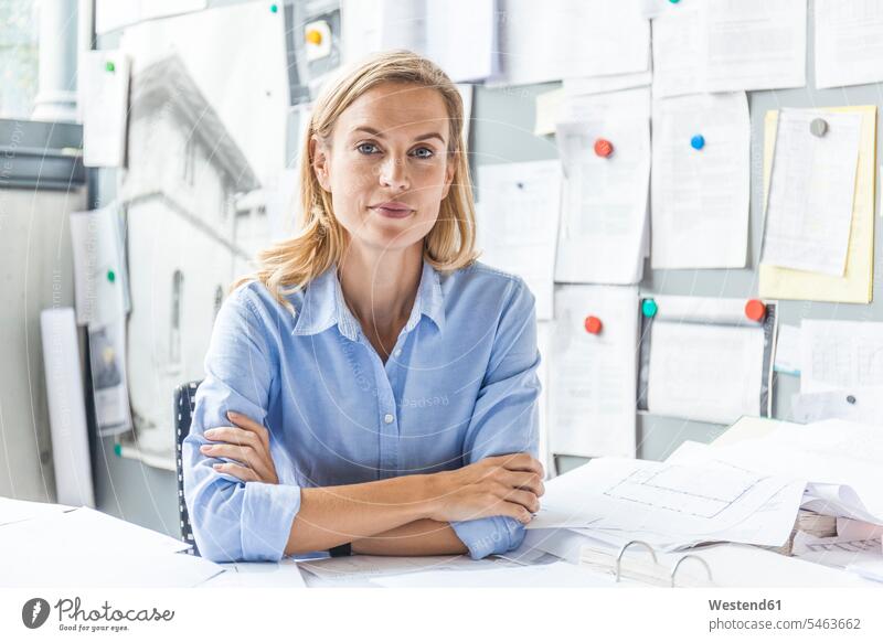 Portrait of confident woman sitting at desk in office surrounded by paperwork offices office room office rooms confidence females women Seated Paperwork