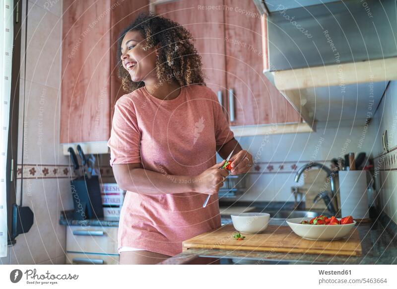 Cheerful young woman looking away while chopping strawberries on kitchen counter at home color image colour image Spain leisure activity leisure activities