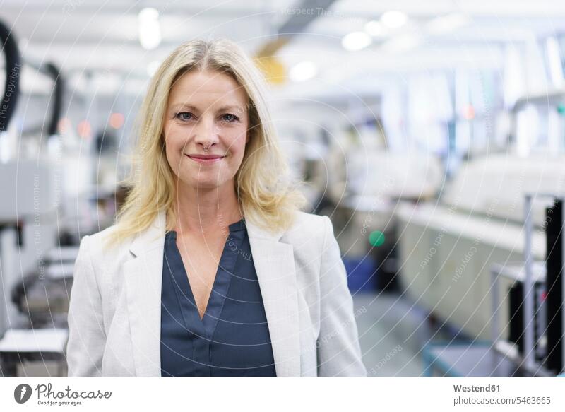 Smiling mature blond businesswoman in businesswear standing at illuminated industry color image colour image indoors indoor shot indoor shots interior