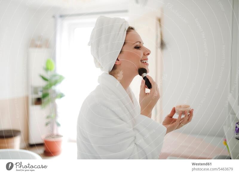 Smiling woman in bathrobe applying make-up in the morning at home smiling smile Makeup Make-up Paint applying makeup painting face bath robes bathrobes females