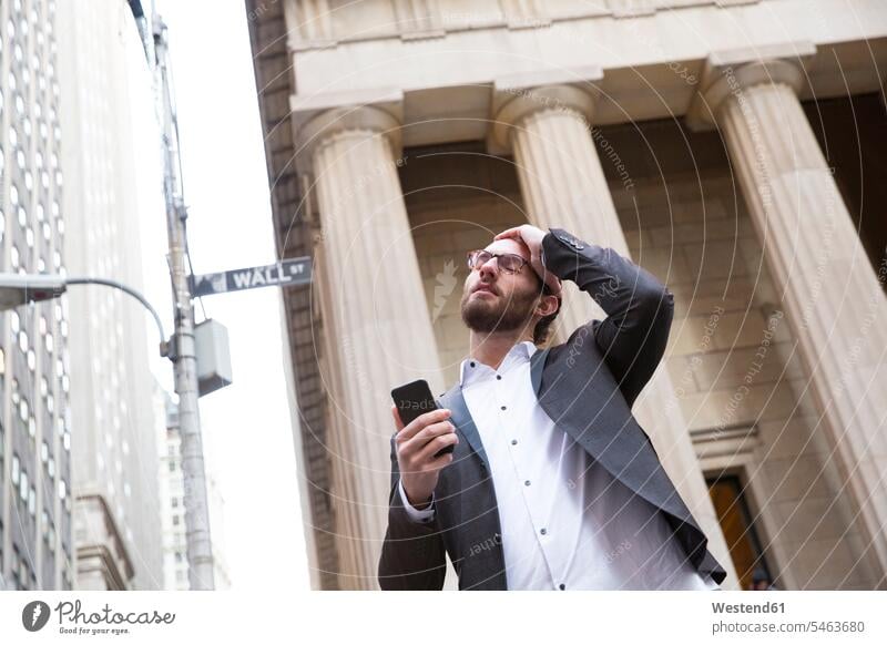Portrait of worried young businessman with cell phone in front of Stock Exchange, New York City, USA business life business world business person businesspeople