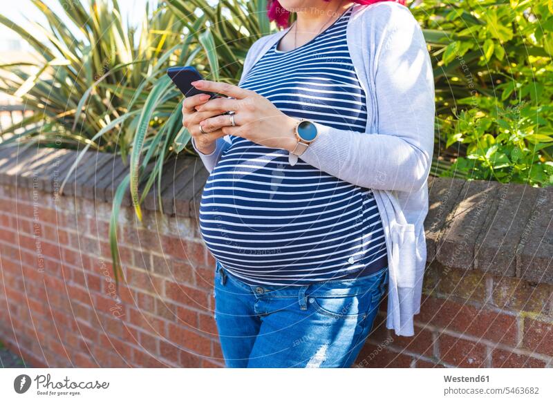 Pregnant woman typing on her phone outside upper part of the body bellies stomach stomachs telecommunication phones telephone telephones cell phone cell phones