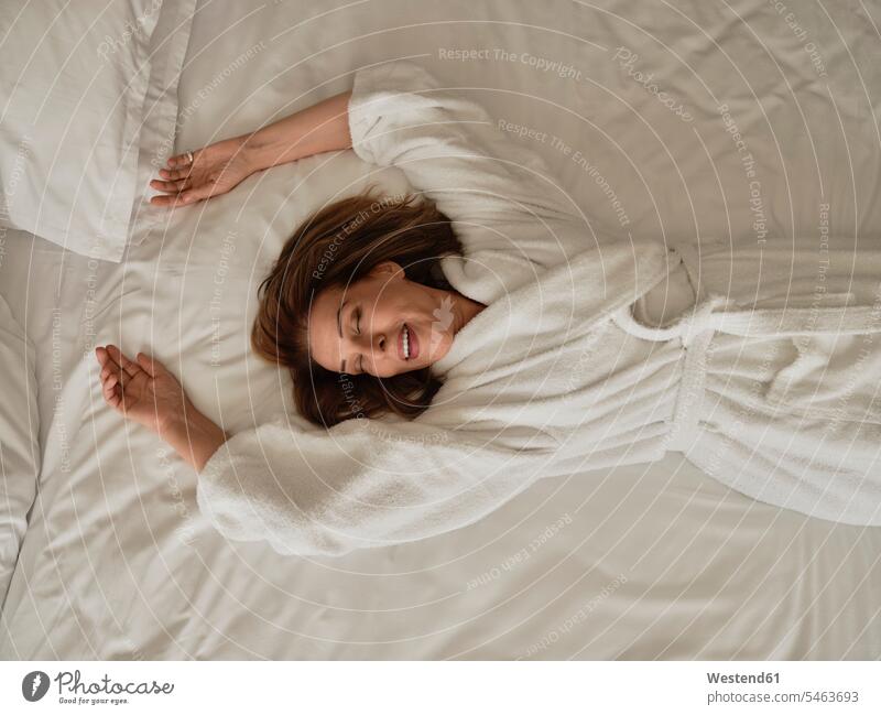 Smiling senior woman lying on white bed at luxury hotel room color image colour image indoors indoor shot indoor shots interior interior view Interiors day