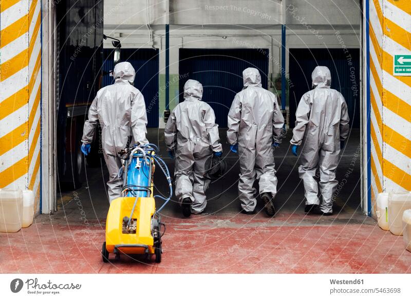 Rear view of sanitation coworkers entering warehouse with decontamination chemical color image colour image Corona Virus Coronavirus disease Covid-19 COVID19
