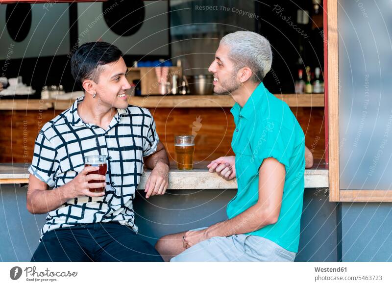 Smiling gay couple talking while drinking beer at bar counter color image colour image outdoors location shots outdoor shot outdoor shots day daylight shot