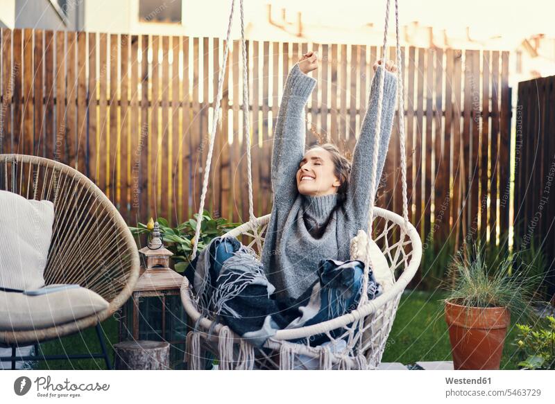 Happy young woman with arms raised relaxing on swing in yard color image colour image leisure activity leisure activities free time leisure time outdoors