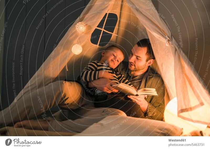 Father reading book to son at an illuminated tent at home books tents Light father pa fathers daddy dads papa sons manchild manchildren parents family families