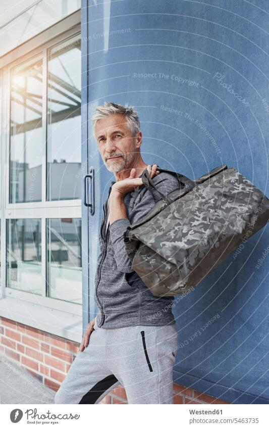 Portrait of mature man with camouflage sports bag standing in front of gym portrait portraits men males gyms Health Club Gym Bag Adults grown-ups grownups adult