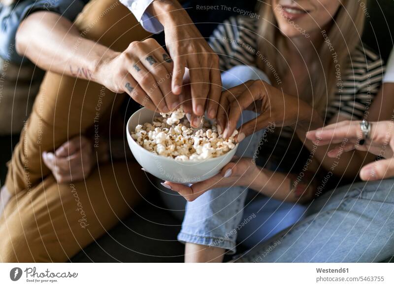 Close-up of friends sitting on couch sharing a bowl of popcorn Seated eating Popcorn Popcorns Bowl Bowls settee sofa sofas couches settees friendship Sweets