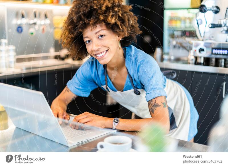Happy female owner using laptop at counter in coffee shop color image colour image indoors indoor shot indoor shots interior interior view Interiors day