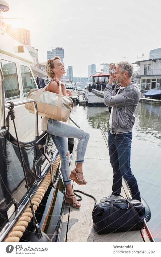 Older man taking picture of young woman on jetty next to yacht jetties standing travelling bag travelling bags traveling bags Yacht Yachts photographing couple