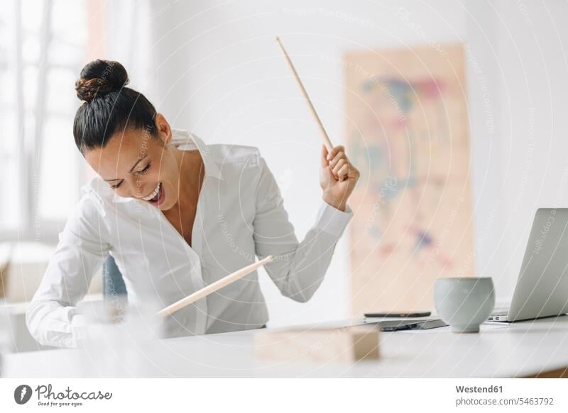 Cheerful female entrepreneur playing drumsticks on desk while screaming in home office color image colour image Germany indoors indoor shot indoor shots