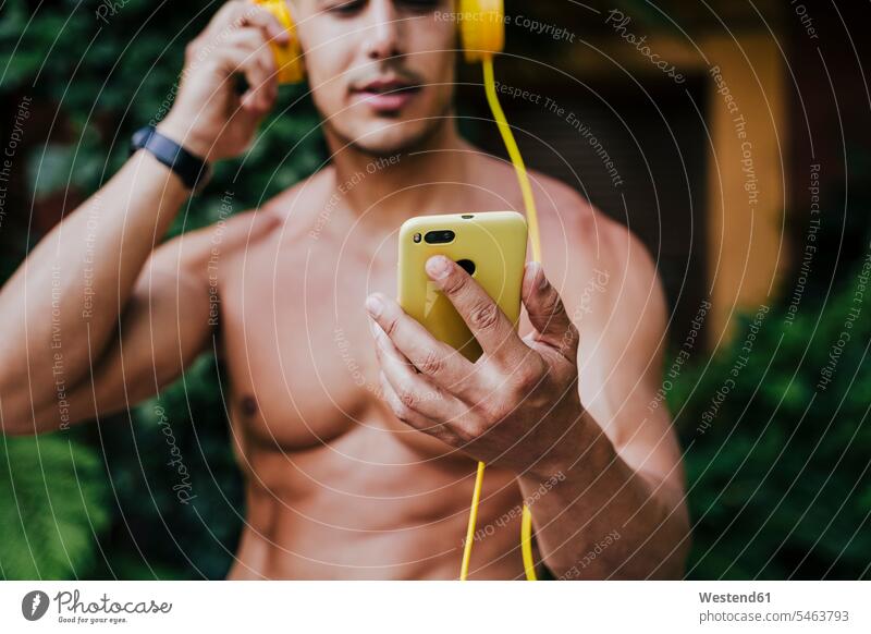 Close-up of shirtless man listening music through headphones while standing in yard color image colour image Spain outdoors location shots outdoor shot