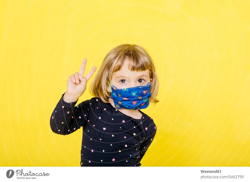 Portrait of cute blond girl wearing face mask and gesturing peace sign against yellow background color image colour image coloured background colored background