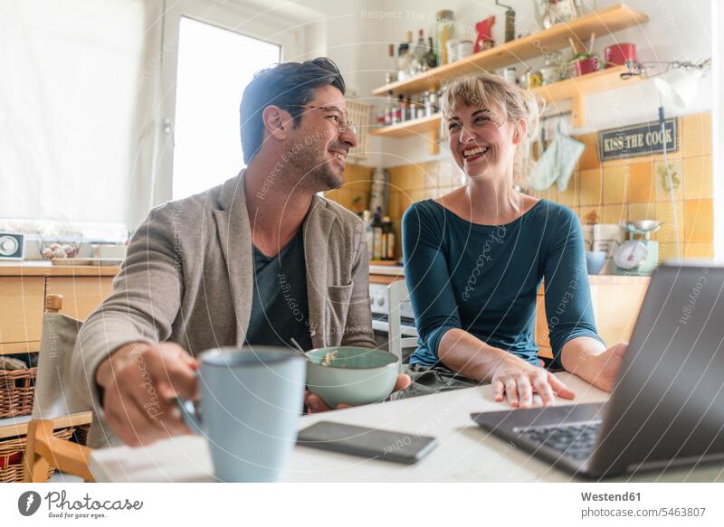 Happy couple sitting at table in kitchen using laptop Bowls windows computers Laptop Computer Laptop Computers laptops notebook telecommunication phones