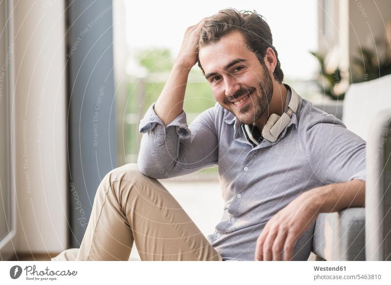 Portrait of young man sitting in his livingroom, with hand in hair caucasian caucasian ethnicity caucasian appearance european friendly nice toothy smile