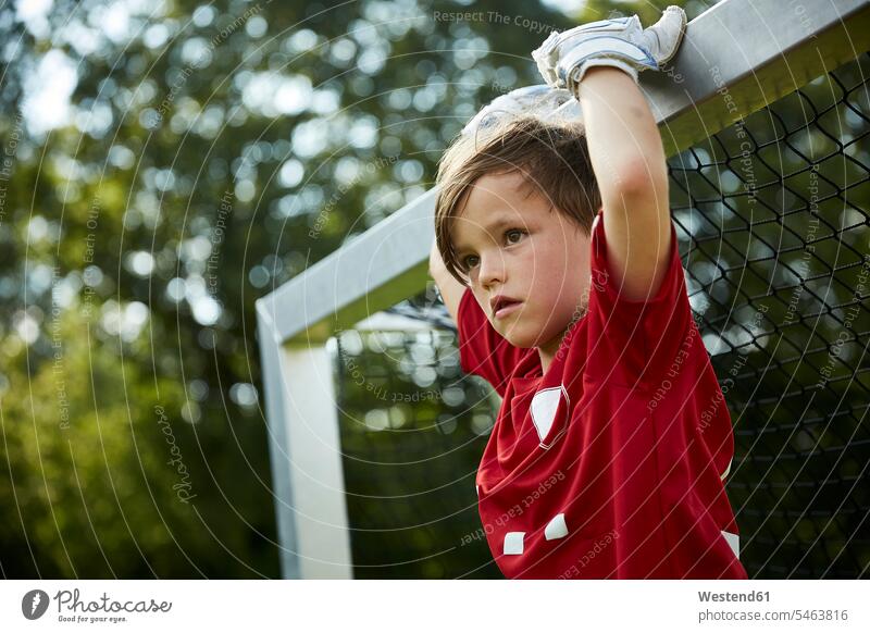 Thoughtful soccer boy holding goal post at field color image colour image outdoors location shots outdoor shot outdoor shots day daylight shot daylight shots