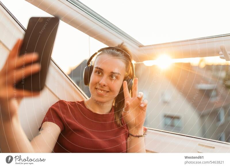 Young woman having a video chat at the window in backlight windows T- Shirt t-shirts tee-shirt headphone headset telecommunication phones telephone telephones