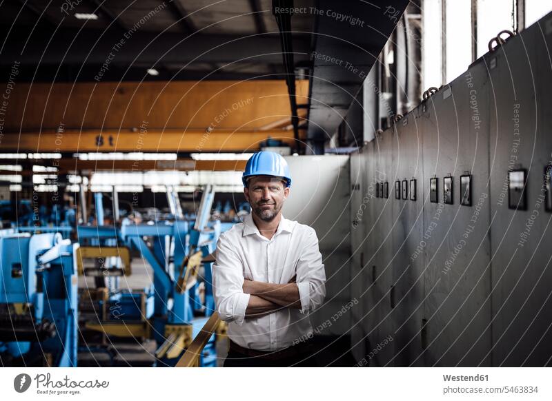 Smiling businessman with arms crossed standing in factory color image colour image indoors indoor shot indoor shots interior interior view Interiors steel mill