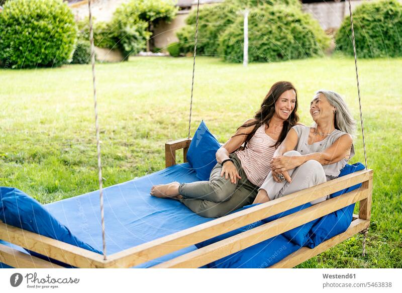 Two happy women relaxing on a hanging bed in garden relaxed relaxation woman females hammock hammocks female friends beds gardens domestic garden happiness