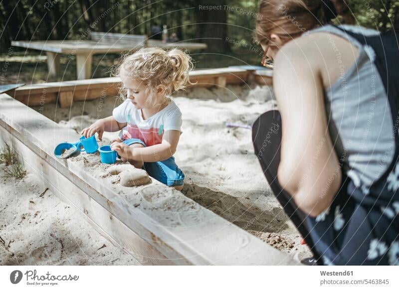 Mother playing with little daughter in sandbox on a playground sandpits sand-box sandboxes sand-boxes play yard play ground playgrounds mother mommy mothers ma