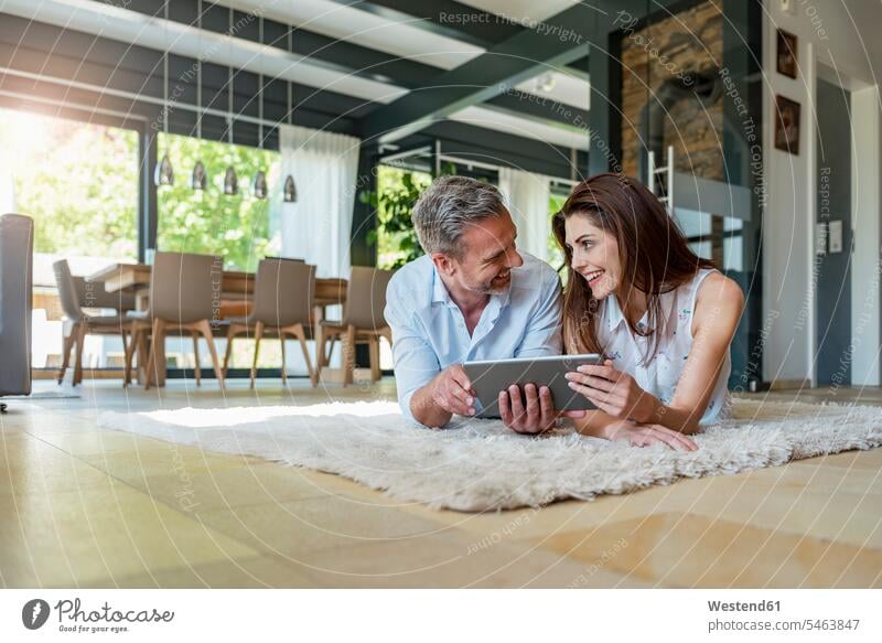 Happy couple lying on carpet at home sharing a tablet carpets rug rugs twosomes partnership couples share laying down lie lying down happiness happy digitizer