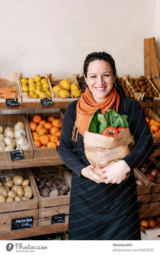 Cheerful saleswoman holding bag of vegetables standing against boxes at store Freshness fresh healthy eating nutrition healthy nutrition diet nourishment