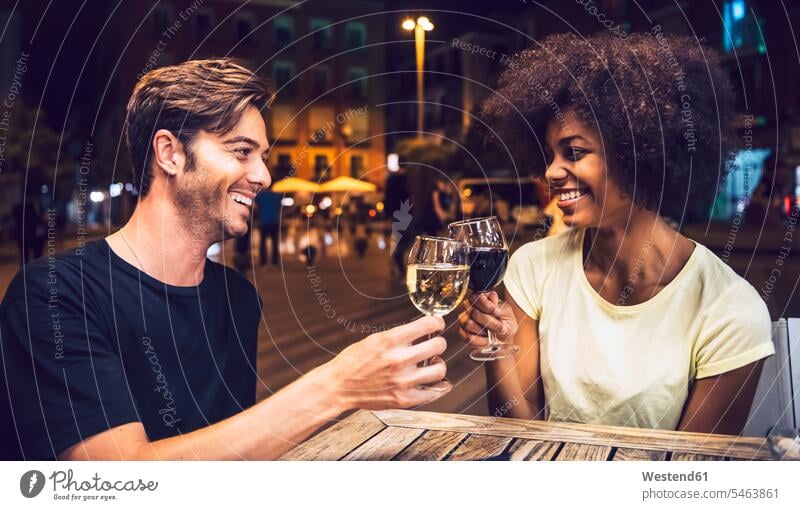 Cheerful couple looking at each other while toasting wineglasses at date night color image colour image Spain leisure activity leisure activities free time
