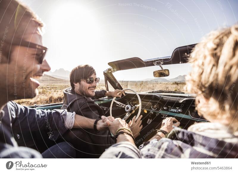 Happy friends in convertible car on a road trip mate touristic tourists motor vehicles road vehicle road vehicles Auto automobile Automobiles cars motorcar