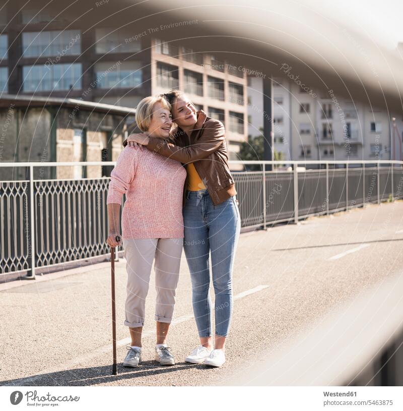 Granddaughter and her grandmother standing on footbridge generation jumper sweater Sweaters smile embrace Embracement hug hugging delight enjoyment Pleasant