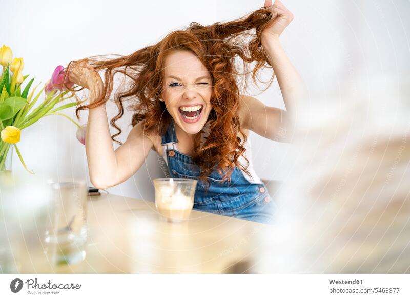 Portrait of cheerful woman pulling hair while sitting with drink at table in room beautiful Woman beautiful Women Beautiful People Handsome People Beauty