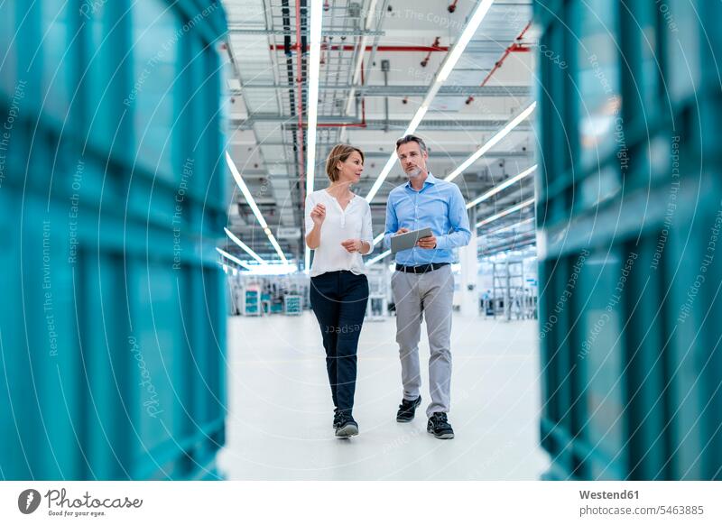 Businessman and businesswoman with tablet talking in a factory hall colleague associate associates partner partners partnerships Occupation Work job jobs