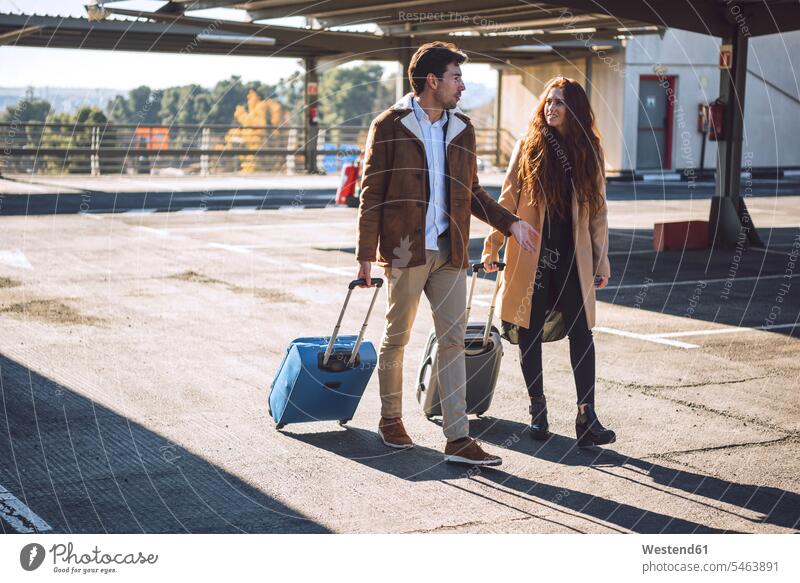 Business couple pulling luggage while walking at airport parking lot color image colour image outdoors location shots outdoor shot outdoor shots day