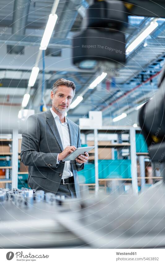 Businessman with tablet in a modern factory hall looking at robot human human being human beings humans person persons caucasian appearance caucasian ethnicity