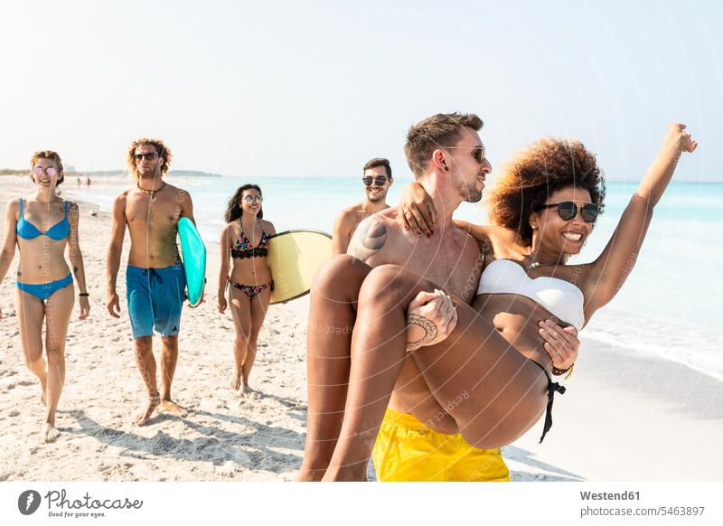 Friends walking on the beach, one man carrying his girlfriend going surfboard surfboards surfer surfers beaches active laughing Laughter Fun having fun funny