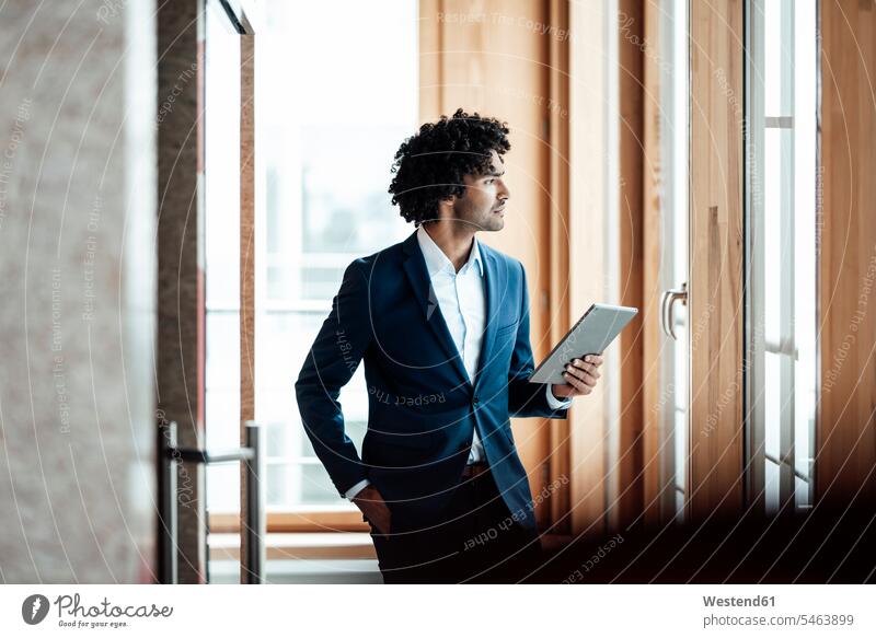 Thoughtful male entrepreneur holding digital tablet while looking away at workplace color image colour image Germany indoors indoor shot indoor shots interior