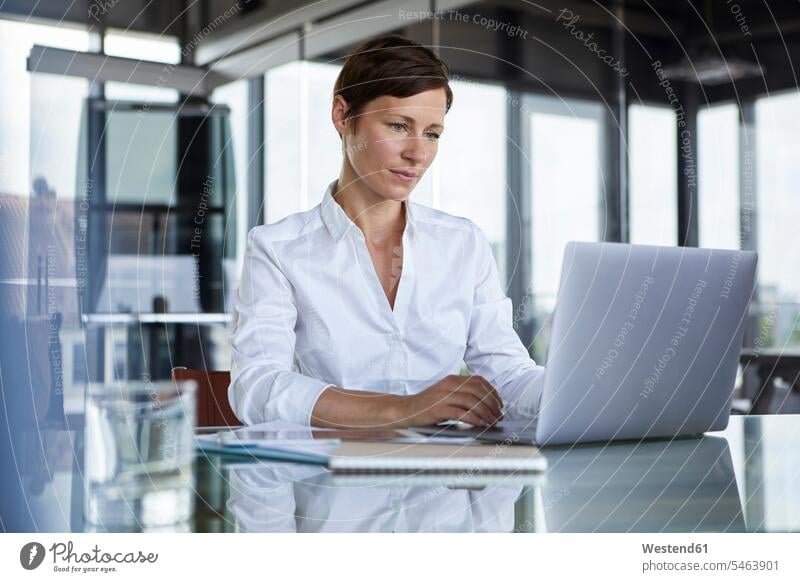 Businesswoman sitting at glass table in office using laptop Seated Laptop Computers laptops notebook businesswoman businesswomen business woman business women
