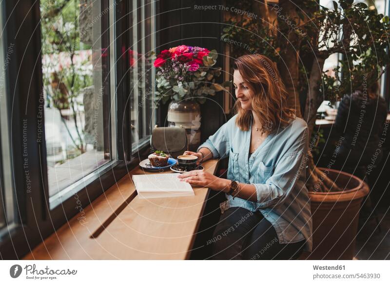 Young woman reading a book in a cafe human human being human beings humans person persons celibate celibates singles solitary people solitary person windows