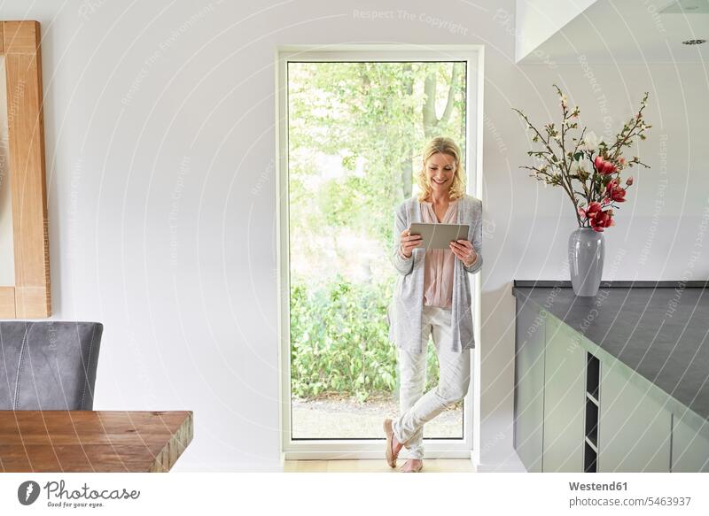 Smiling woman standing at French door using tablet at home females women digitizer Tablet Computer Tablet PC Tablet Computers iPad Digital Tablet