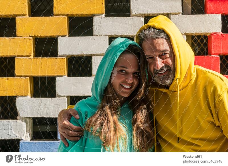 Smiling father and daughter standing against brick wall color image colour image outdoors location shots outdoor shot outdoor shots day daylight shot