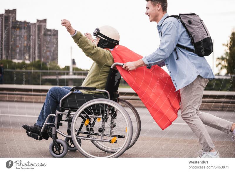 Young man pushing senior man sitting in a wheelchair dressed up as superhero human human being human beings humans person persons caucasian appearance