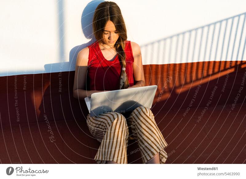 Teenage girl sitting outdoors in sunlight using laptop Seated Laptop Computers laptops notebook Teenage Girls female teenagers Sunlit computer computers