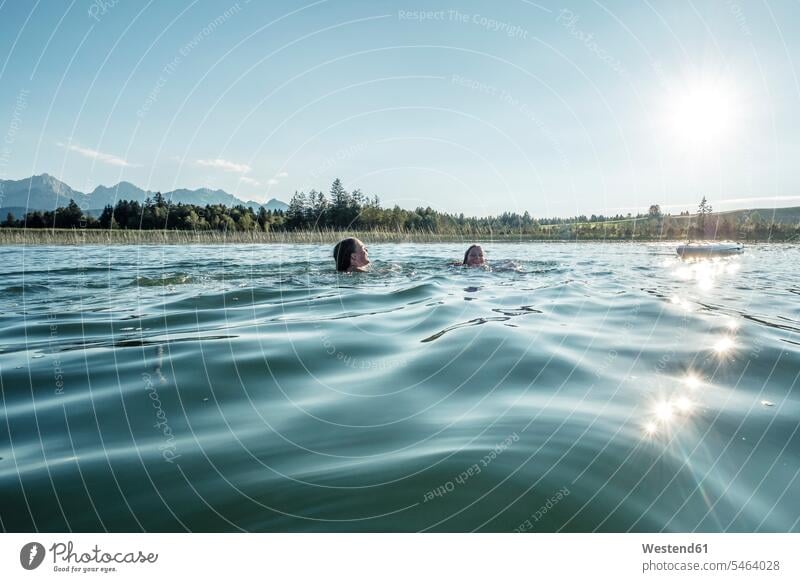 Two girls swimming in a lake in sunshine, Bannwaldsee, Allgaeu, Bavaria, Germany day daylight focus on foreground focus on the foreground blur blurred outdoor