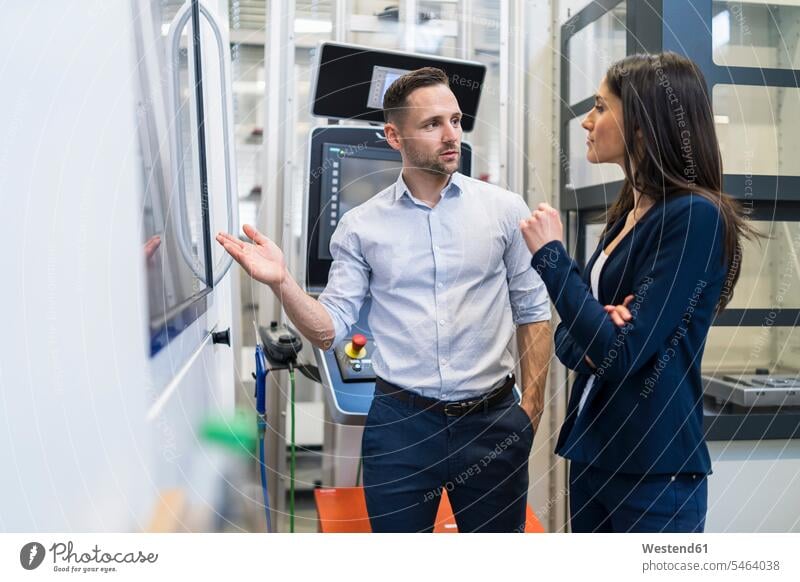 Businessman and businesswoman talking at a machine in modern factory speaking factories Business man Businessmen Business men businesswomen business woman