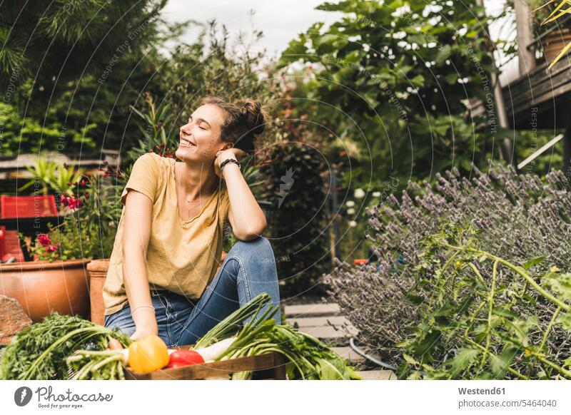 Young woman with eyes closed sitting by vegetables and plants in community garden color image colour image Germany leisure activity leisure activities free time