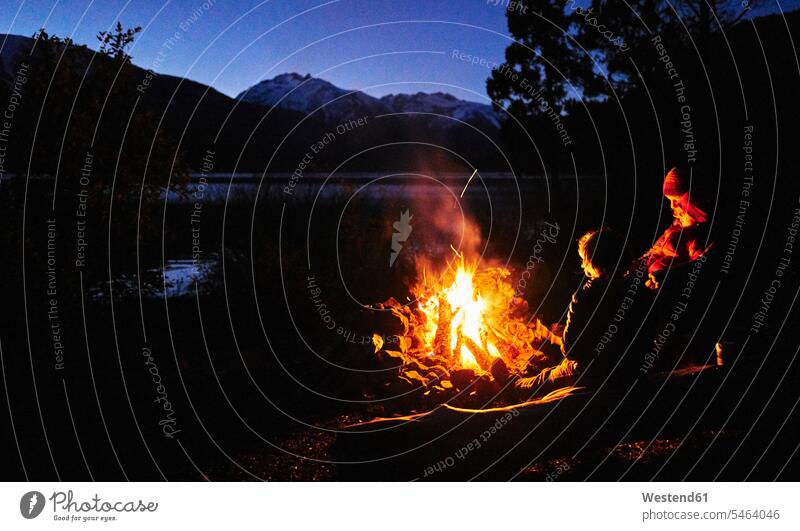 Argentina, Patagonia, Lago Futalaufquen, mother with sons at camp fire at night manchild manchildren mommy mothers mummy mama boy boys males by night nite