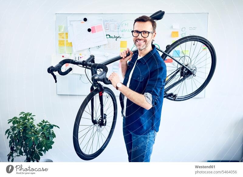 Portrait of smiling businessman carrying bicycle in office smile offices office room office rooms bikes bicycles portrait portraits workplace work place