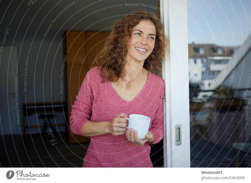 Woman with coffee cup smiling while leaning on door at home color image colour image day daylight shot daylight shots day shots daytime Home Interior