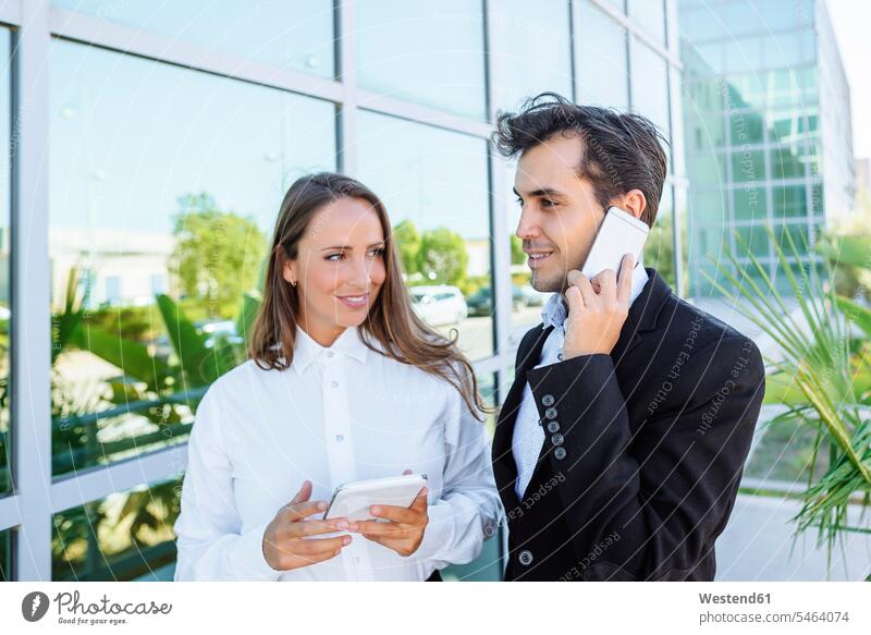 Smiling businesswoman and businessman with tablet and cell phone outside office building businesswomen business woman business women Businessman Business man